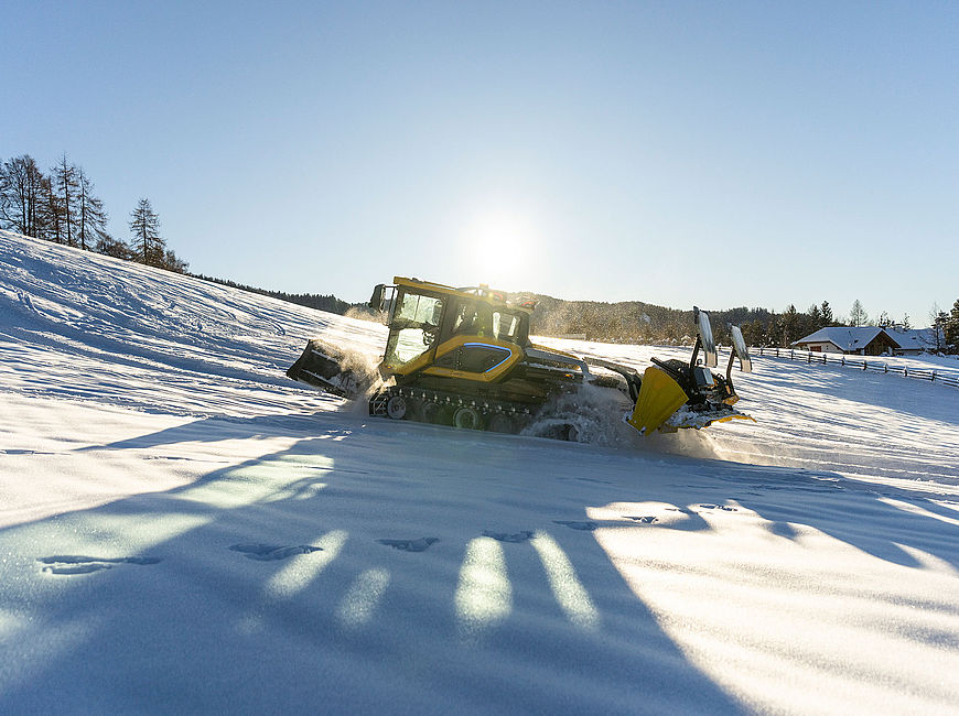 Yellow Xelom SnowCat groomer prepares snowy slope in backlight of winter sun with mountain panorama